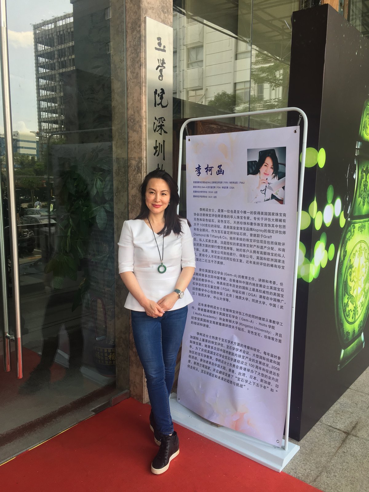 Kehan Li at the entrance of the Shenzhen Jade Institute, beside a tall poster announcing her lecture in Chinese.